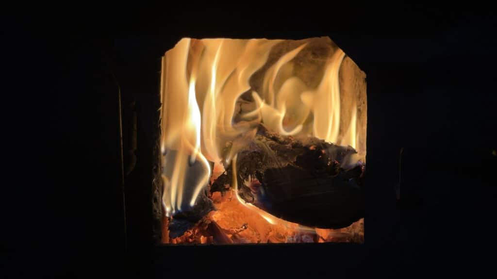 Flammes jaunes et orangées dansant dans un foyer sur bûches de bois incandescentes, braises rouges sur fond noir profond.